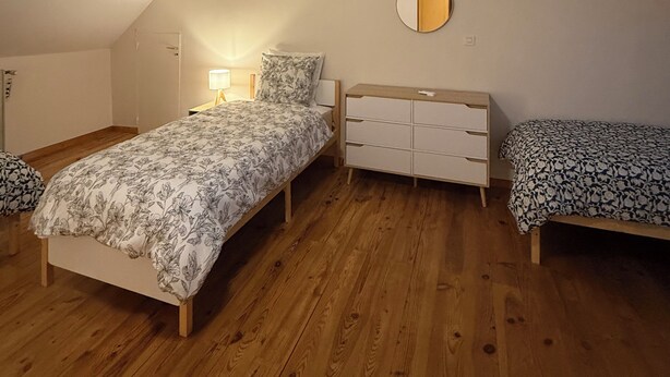 Un dormitorio con ventilador de techo, una cama con ropa de cama floral, una mesita de noche, un aparador y una lámpara de noche pequeña.