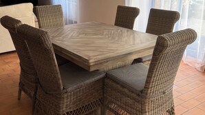 Un comedor con una mesa cuadrada rodeada de sillas de mimbre, una lámpara colgante y vistas a través de una ventana.