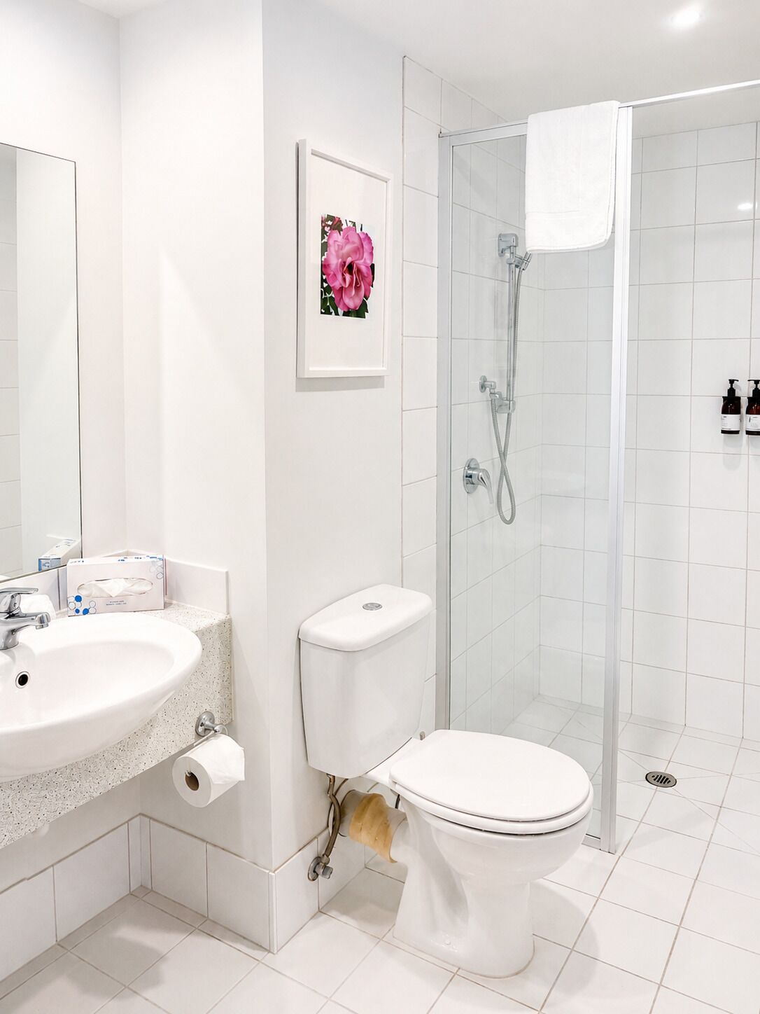 Un baño moderno con lavamanos blanco, inodoro y ducha con mampara de vidrio.