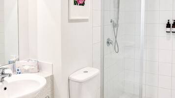 Un baño moderno con lavamanos blanco, inodoro y ducha con mampara de vidrio.