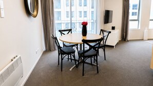 Habitación de hotel con una mesa redonda, cuatro sillas, un jarrón con una flor, un televisor de pantalla plana y un radiador.