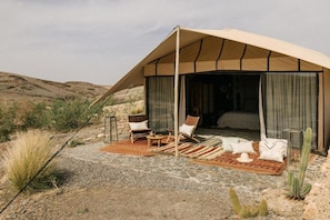 A tented accommodation with a bed, two chairs, a small table, and a cactus in the foreground. - Caravan by Habitas Agafay (Agafay)