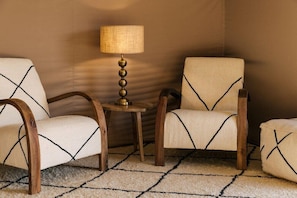 A corner of a room with two upholstered chairs, a small wooden table, and a lamp. - Caravan by Habitas Agafay (Agafay)