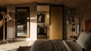 Um quarto com uma cama, um espelho, uma mesa de cabeceira com abajur e vista para outro cômodo.