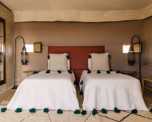 Una cama doble con ropa blanca y pompones verdes, cabecera roja y dos lámparas fijadas a la pared.