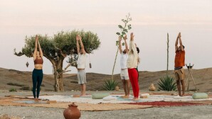 Quatro pessoas praticam yoga em ambiente externo, com árvores e céu claro.