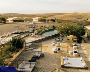 A pool area with lounge chairs and umbrellas, surrounded by desert landscape. - Caravan by Habitas Agafay (Agafay)