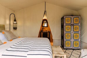 A bedroom with a bed, a hanging light fixture, a cabinet, and a wall-mounted lamp. - Caravan by Habitas Agafay (Agafay)