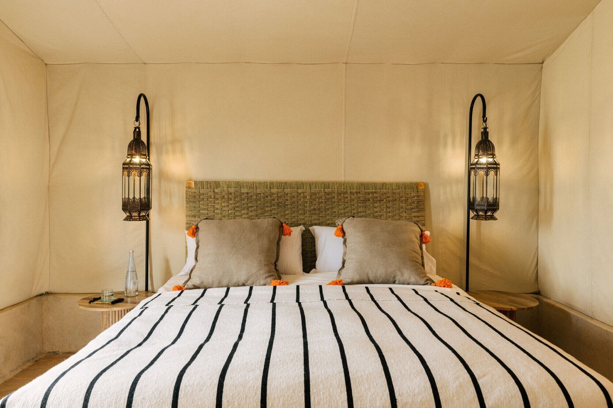 Habitación de hotel con cama, dos mesitas de noche, cabecera de mimbre y dos faroles de pared.