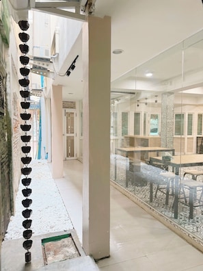 A corridor with a series of black hanging objects, a glass partition, and a tiled floor. - Via Si Phraya (Bangkok)