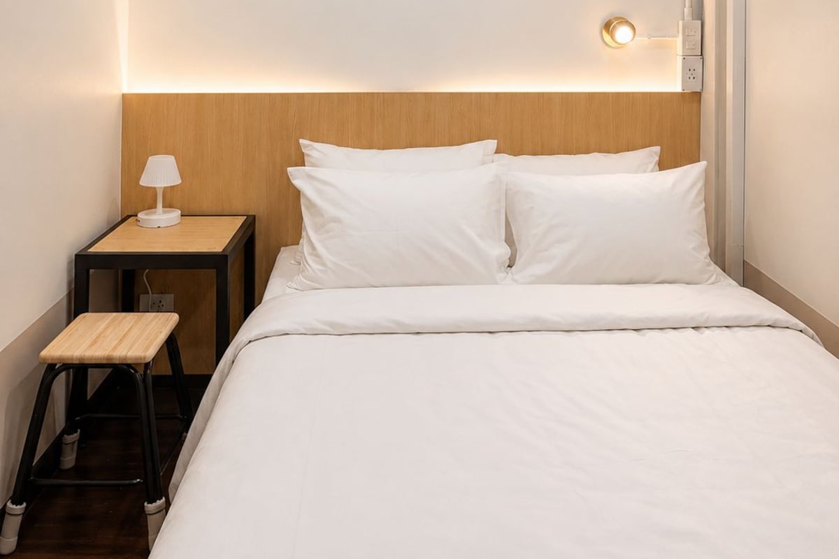 A hotel room with a bed, a nightstand, a lamp, and a wall-mounted light fixture.