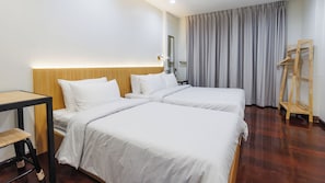 A hotel room with two beds, a wooden headboard, a bedside table, a mirror, a wooden hanger, and a window with curtains. - Via Si Phraya (Bangkok)