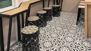 Una habitación con una mesa larga, cuatro sillas, un televisor montado en la pared y baldosas de suelo estampadas.