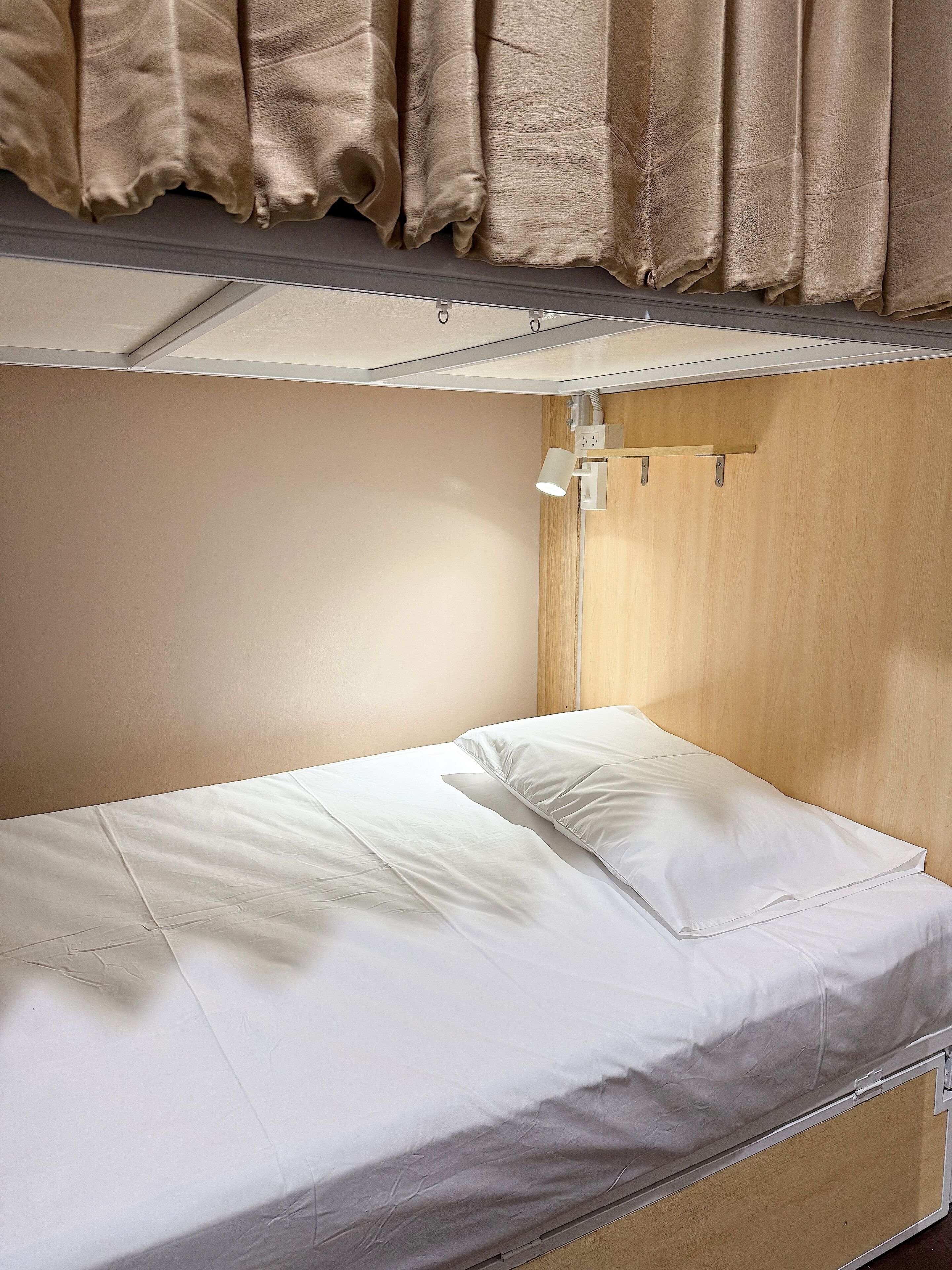 Un lit superposé avec une tête de lit, un bureau escamotable et une fenêtre avec des rideaux.