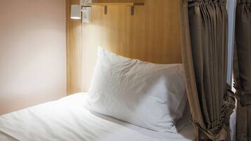 Uma cama com roupa de cama branca, cabeceira de madeira e cortina.