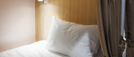 A bed with white bedding, a wooden headboard, and a curtain.