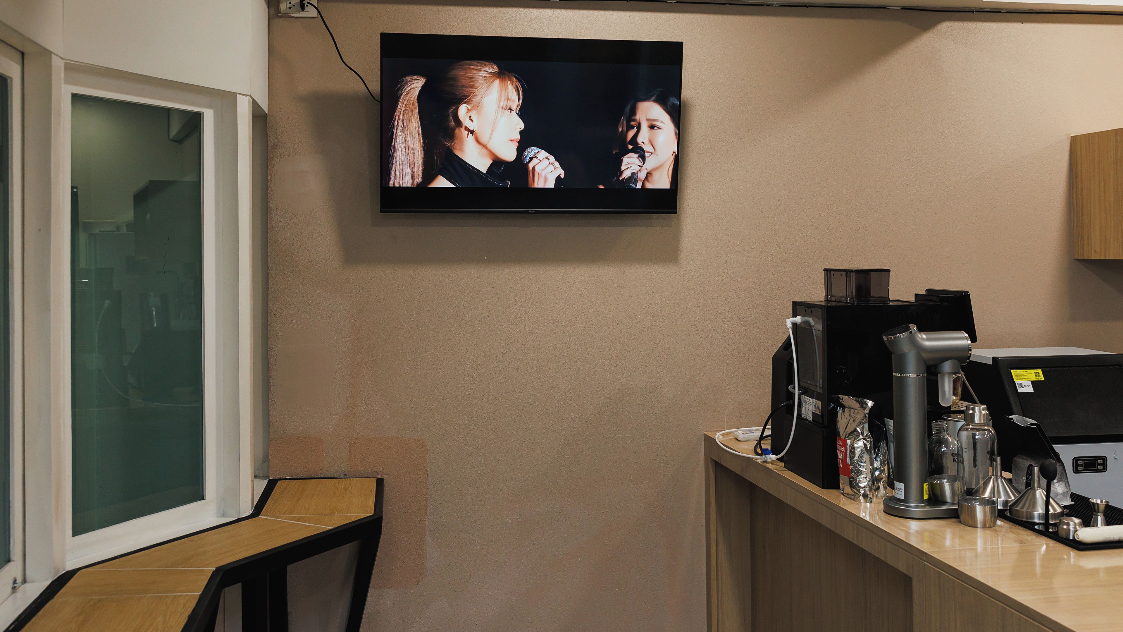A kitchen area with a coffee machine, a television mounted on the wall, and a window with a view.