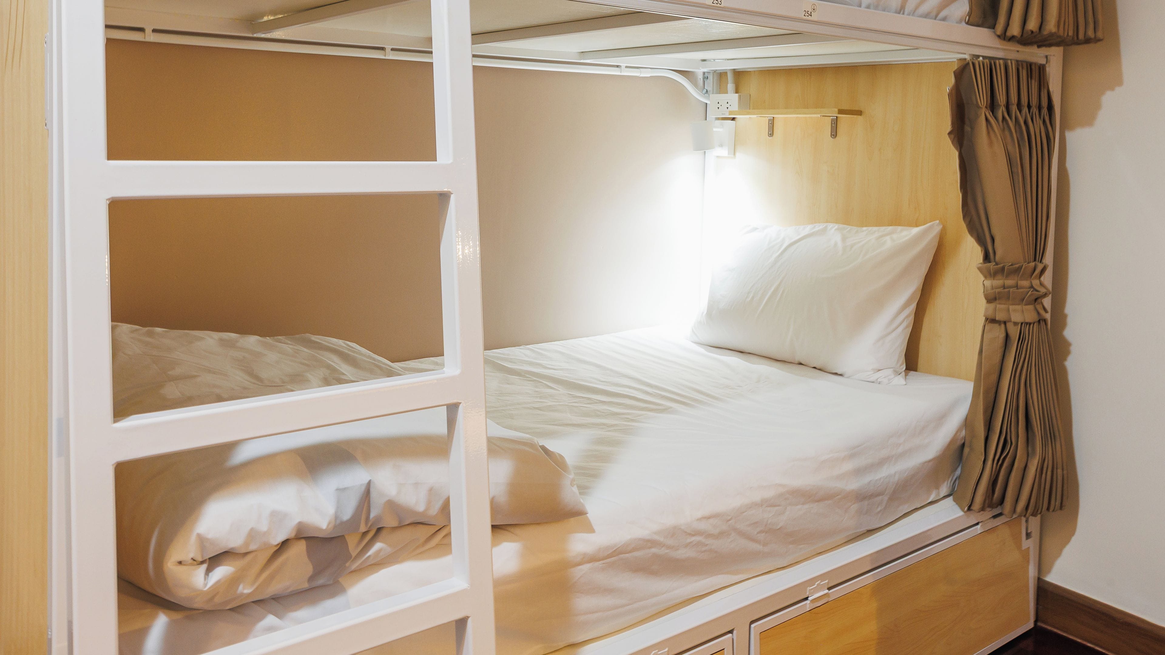 A bunk bed with a wooden frame, white bedding, and a curtain on the right side.