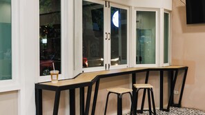 A corner seating area with a counter and stools, a drink on the counter, and a view through the window. - Via Si Phraya (Bangkok)