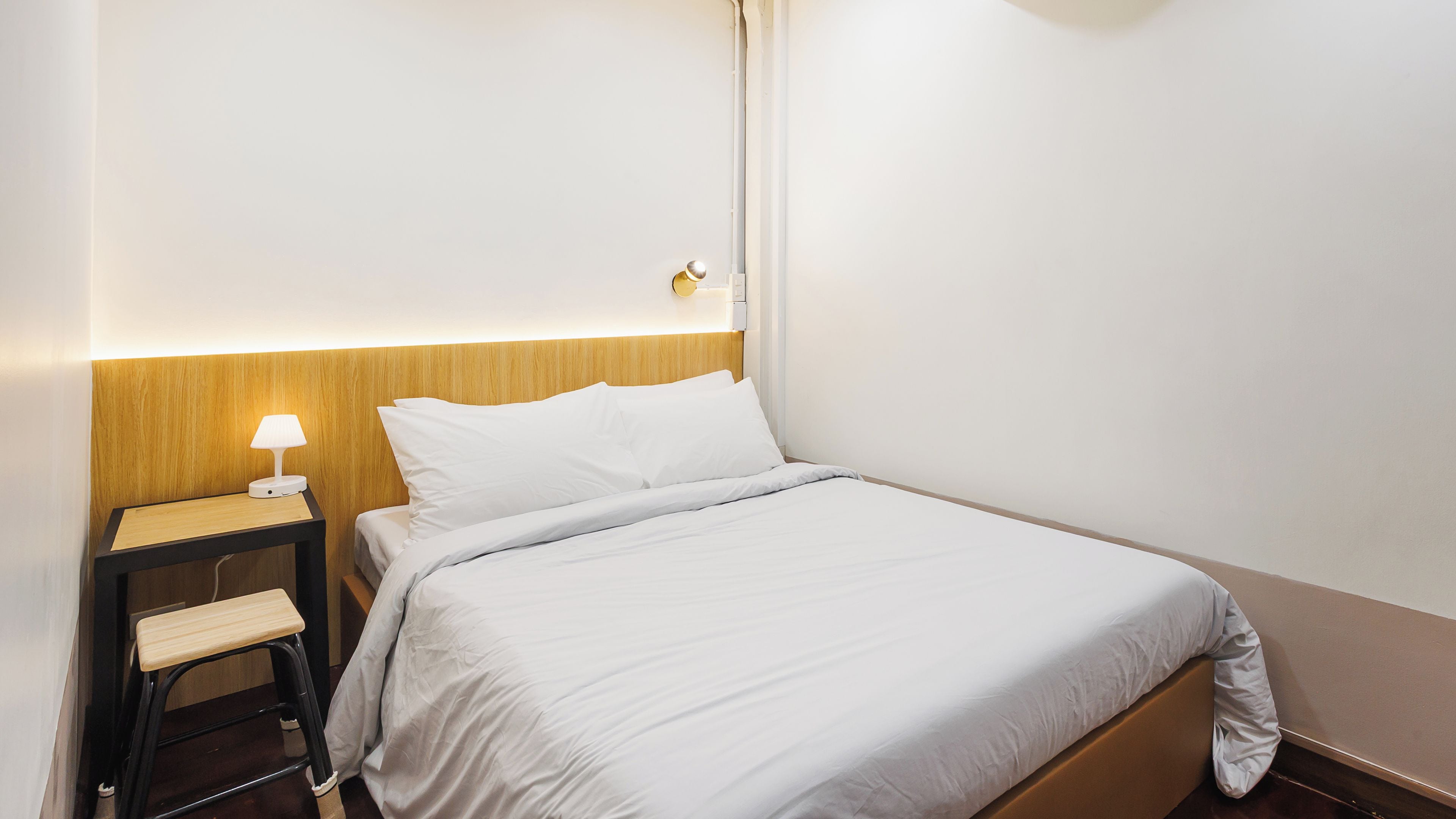 A neatly made bed with white bedding, a bedside table with a lamp, and a wooden headboard.