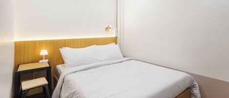 A neatly made bed with white bedding, a bedside table with a lamp, and a wooden headboard.