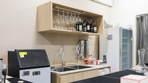 A kitchenette with a refrigerator, a coffee machine, a sink, and a wine rack with bottles and glasses. - Via Si Phraya (Bangkok)