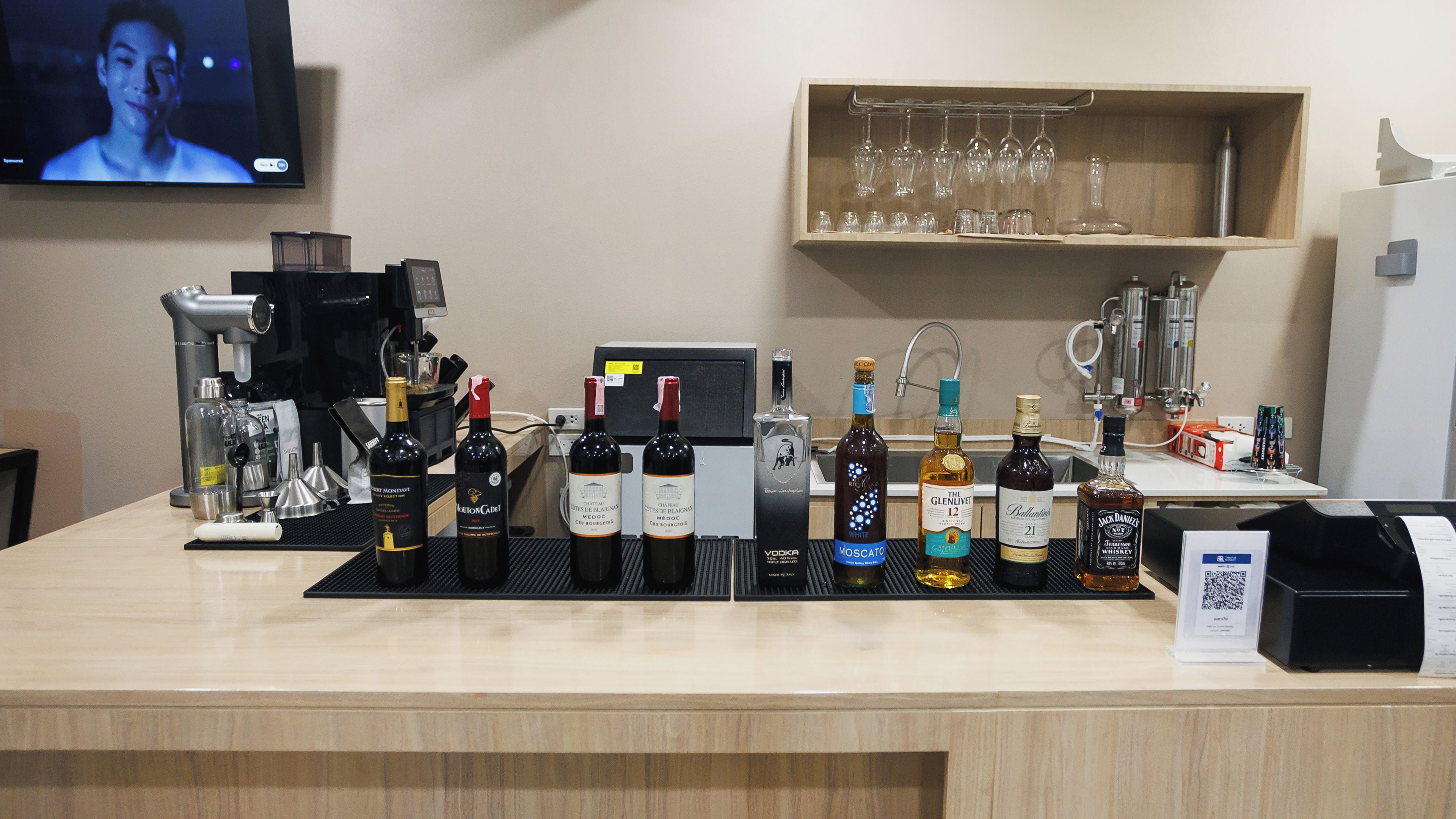 A bar area with a selection of alcohol bottles, a coffee machine, and a television screen in the background.