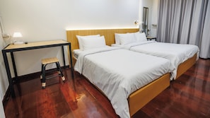 A hotel room with two single beds, a small table with a lamp, and a wooden desk. - Via Si Phraya (Bangkok)