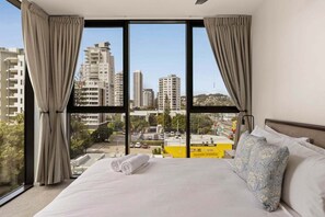 A hotel room with a large bed, curtains, a view of the cityscape, and a window. - Sea Glimpse Escape at Sandbar Burleigh (Gold Coast)