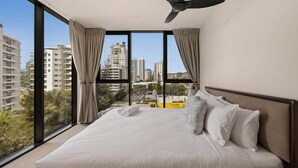 A hotel room with a large bed, a ceiling fan, and a view of the city through floor-to-ceiling windows. - Sea Glimpse Escape at Sandbar Burleigh (Gold Coast)
