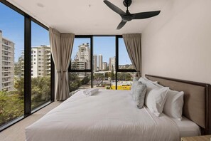 A hotel room with a large bed, a ceiling fan, and a view of the city through floor-to-ceiling windows. - Sea Glimpse Escape at Sandbar Burleigh (Gold Coast)