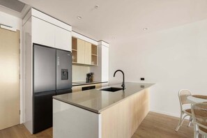 A modern kitchen with a built-in refrigerator, a sink, and a dining area with a table and chairs. - Sea Glimpse Escape at Sandbar Burleigh (Gold Coast)