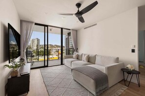 A modern living room with a sofa, a small table, a ceiling fan, and a view through a glass door. - Sea Glimpse Escape at Sandbar Burleigh (Gold Coast)