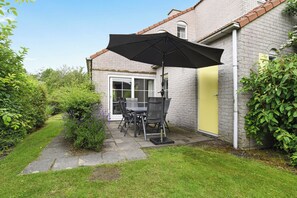 A patio with a table and chairs, a black umbrella, and a brick house with a yellow door. - Easygoing Garden Stay in Brouwershaven (Brouwershaven)