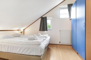 A bedroom with a bed, a window with curtains, a radiator, and a blue wardrobe. - Easygoing Garden Stay in Brouwershaven (Brouwershaven)