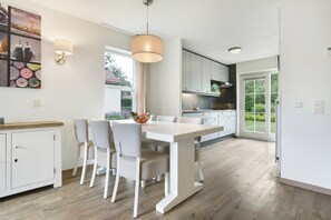 A modern kitchen with a dining area, featuring a large island, pendant lighting, and a view of the outdoors. - Easygoing Garden Stay in Brouwershaven (Brouwershaven)
