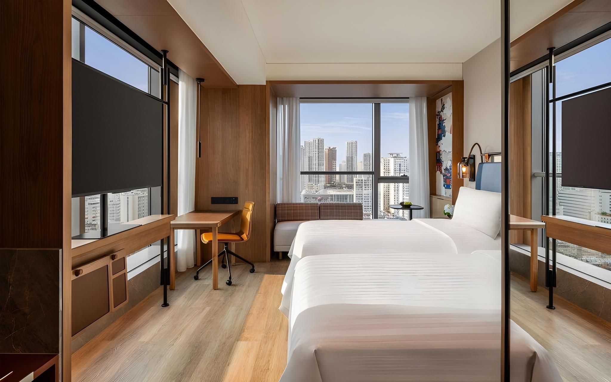 A hotel room with a large bed, a desk, and a view of the cityscape.
