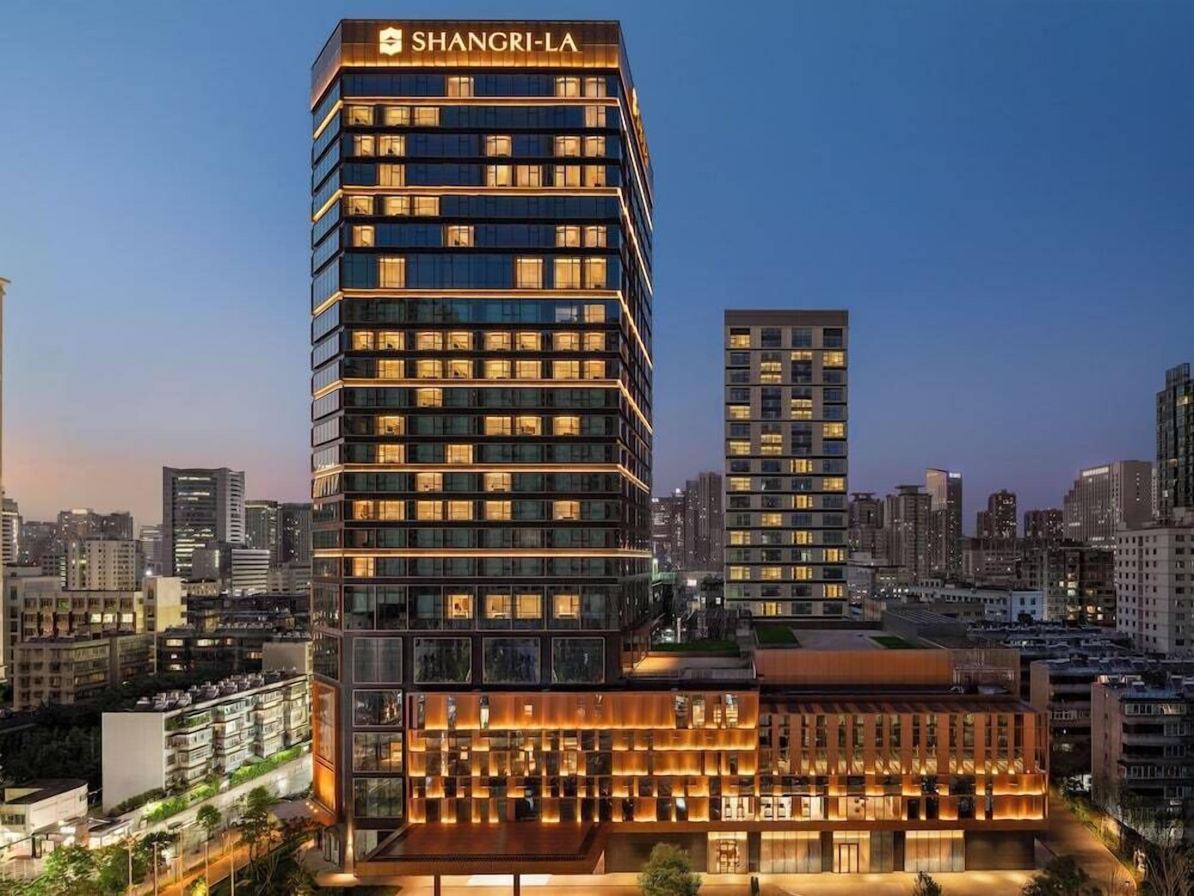 A modern hotel with a prominent 'SHANGRI-LA' sign, multiple floors, and a well-lit facade.