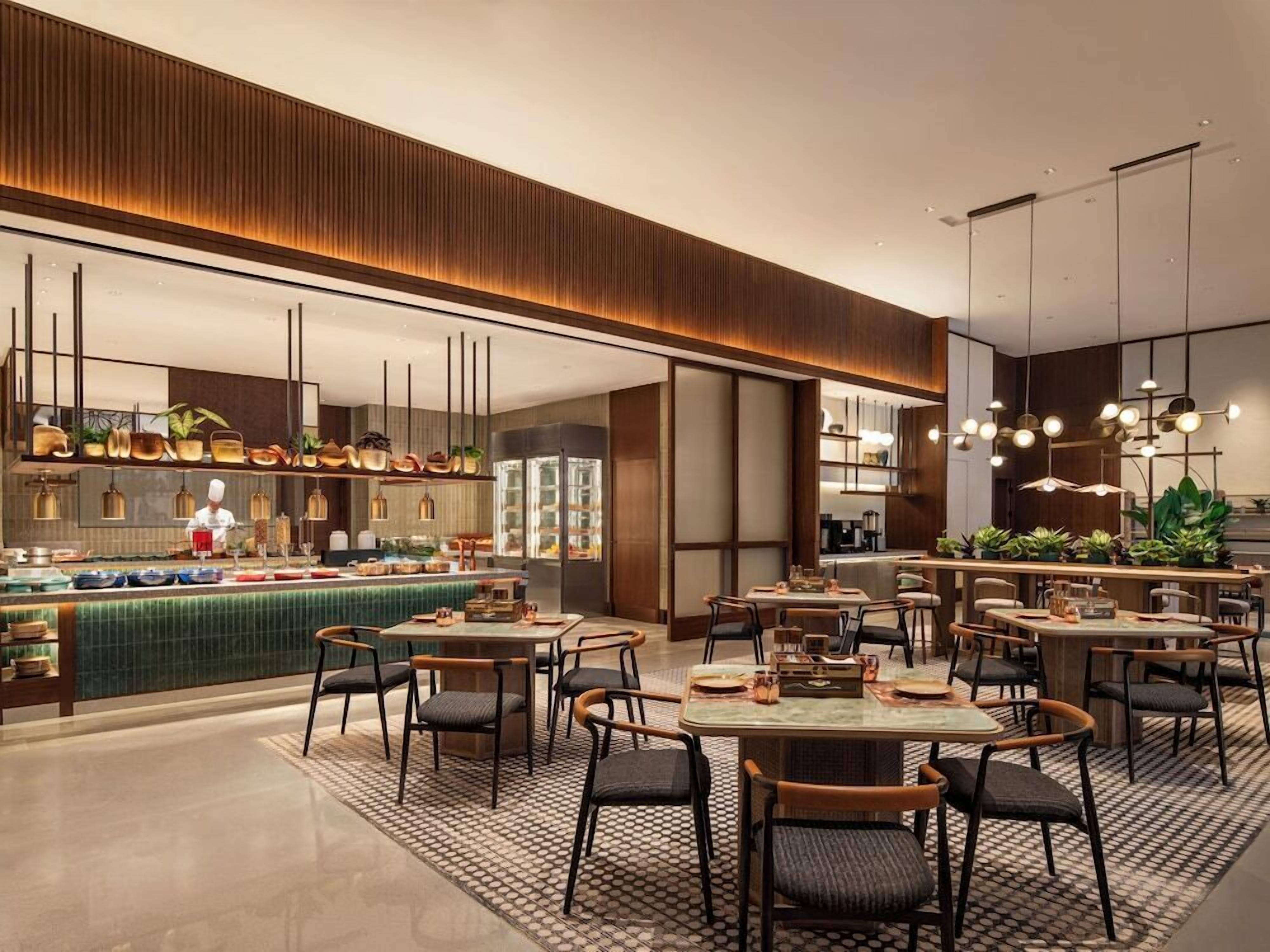 A modern restaurant with a bar area, multiple dining tables, and a chef preparing food.