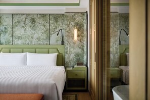 Habitació d'hotel amb un llit gran, una tauleta de nit amb una làmpada i una paret amb un disseny texturat.