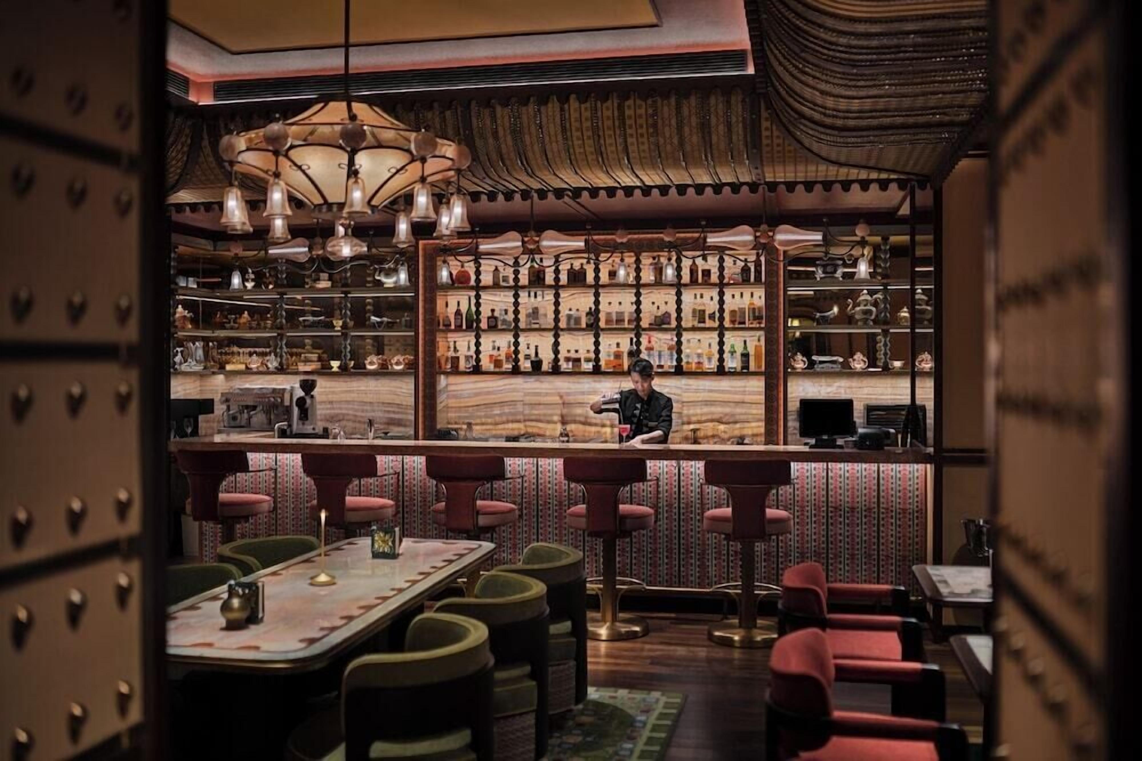 Un espace bar avec un barman, des étagères remplies de bouteilles et un mur décoré de motifs.