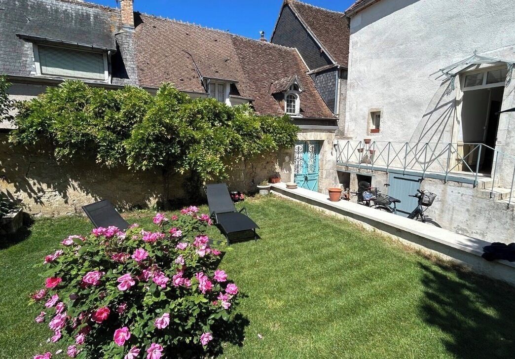 A courtyard with a lawn, a rose bush, and a building with a tiled roof.