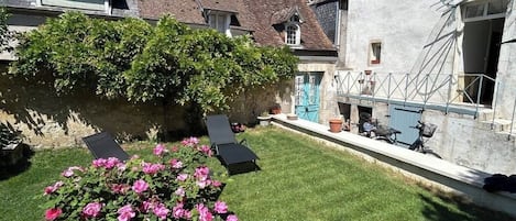 A courtyard with a lawn, a rose bush, and a building with a tiled roof.