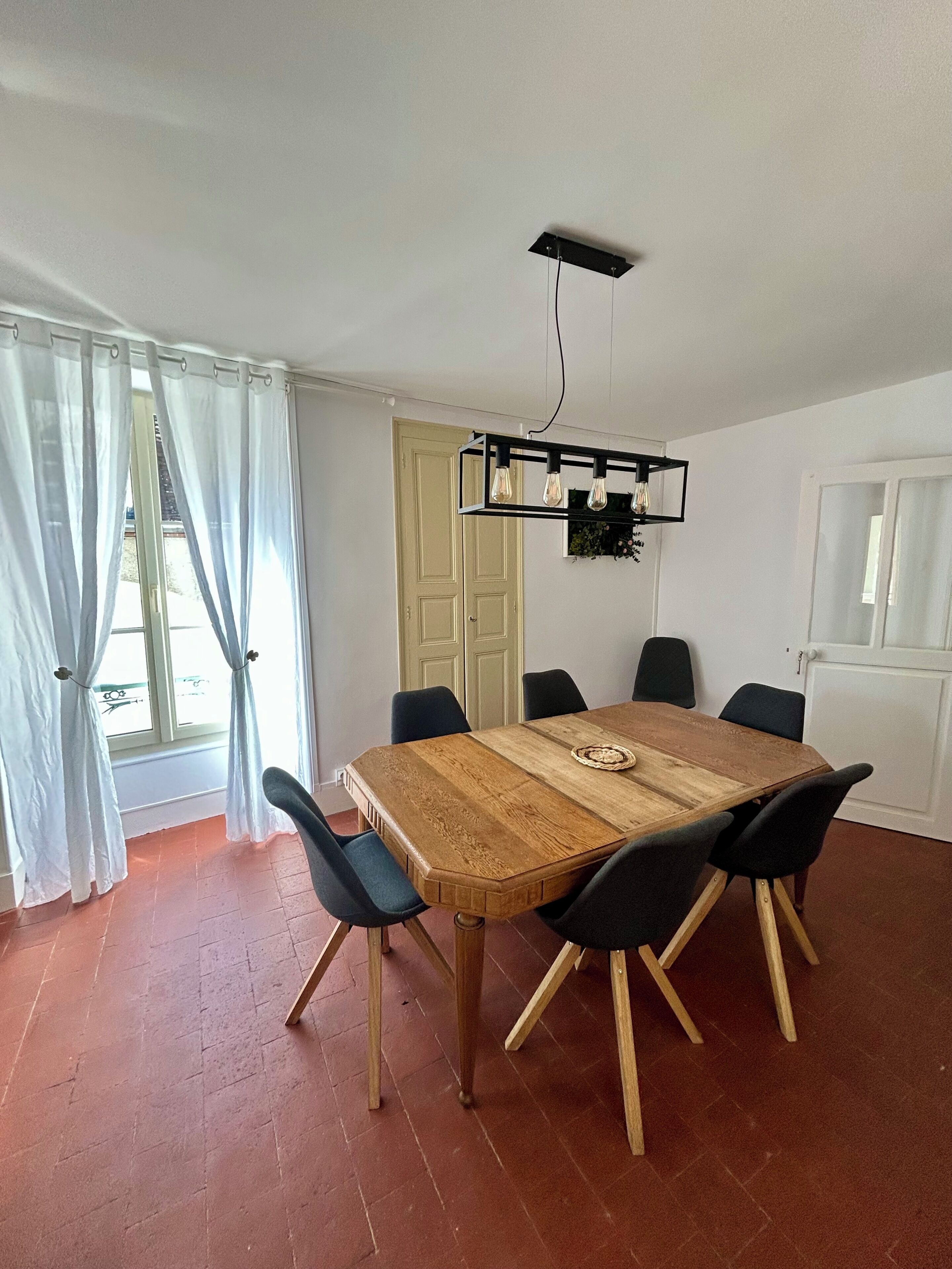 Un comedor con una mesa de madera, seis sillas, una lámpara colgante y una puerta al fondo.