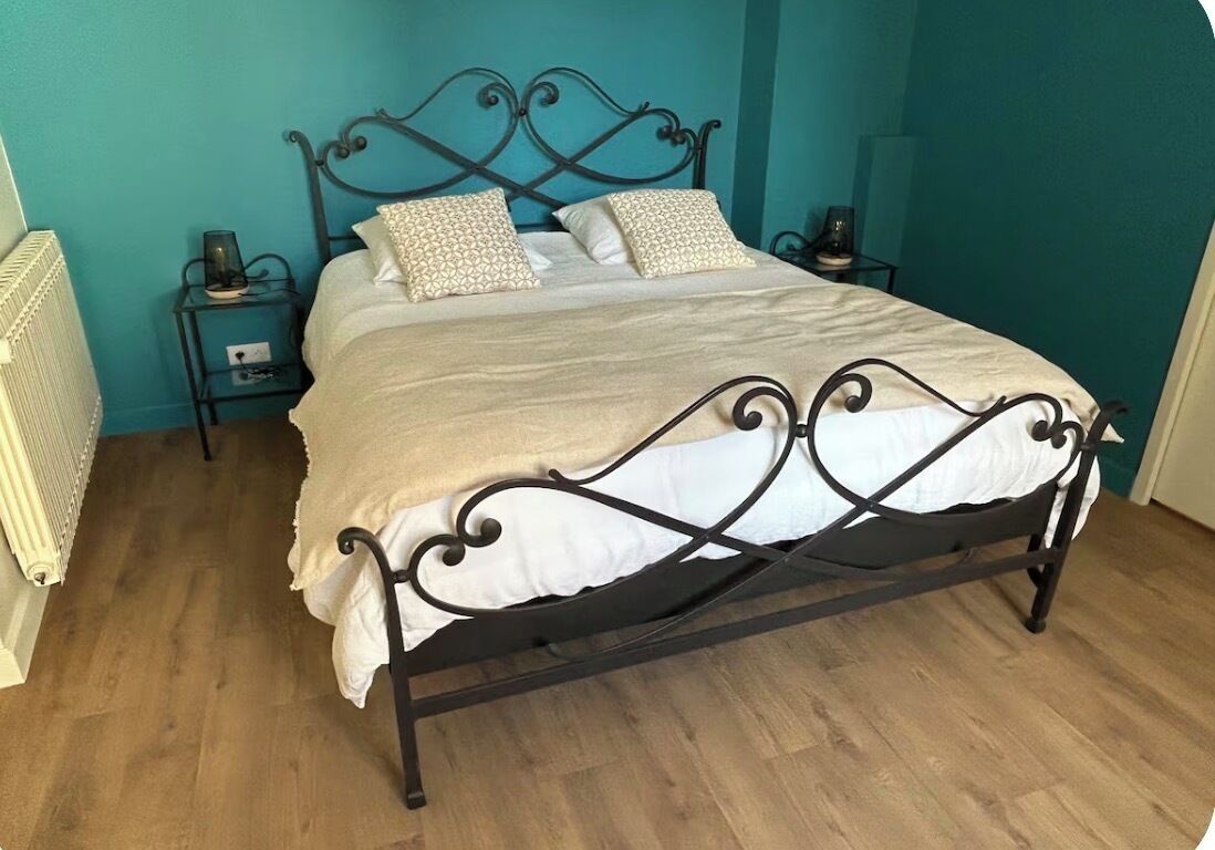 A bed with a metal frame and white bedding, a nightstand with a lamp, and a radiator on the left.
