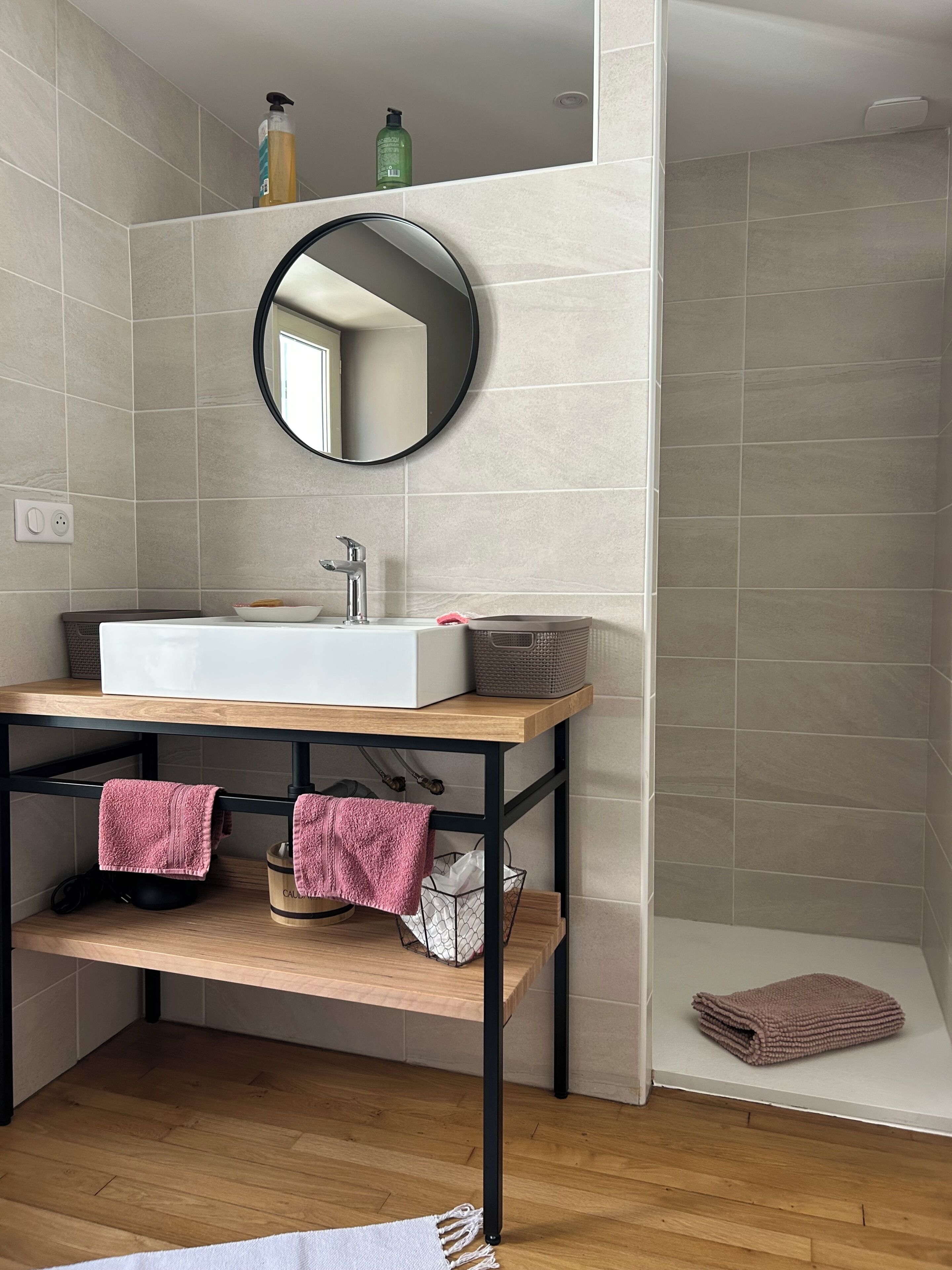 Une salle de bain moderne avec un lavabo blanc, un miroir rond et un meuble-lavabo en bois.