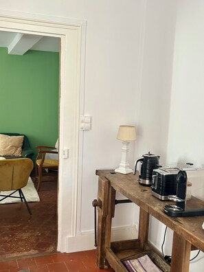 Ett rum med ett träbord där det står en lampa, en vattenkokare och en brödrost. Det finns en grön vägg och en dörr som leder till ett annat rum.