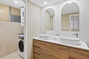 Ein modernes Badezimmer mit einem Doppelwaschbecken, einer Waschmaschine, Holzschränken und einem großen Spiegel.