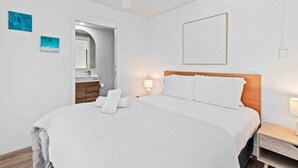 Ein Hotelzimmer mit Bett, Deckenventilator, Nachttisch, Spiegel und Kunstwerken an den Wänden.