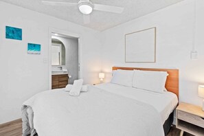 A hotel room with a bed, a ceiling fan, a nightstand, a mirror, and artwork on the walls. - Wyuna Coastal Escape - 3BR Apartment (Gold Coast)